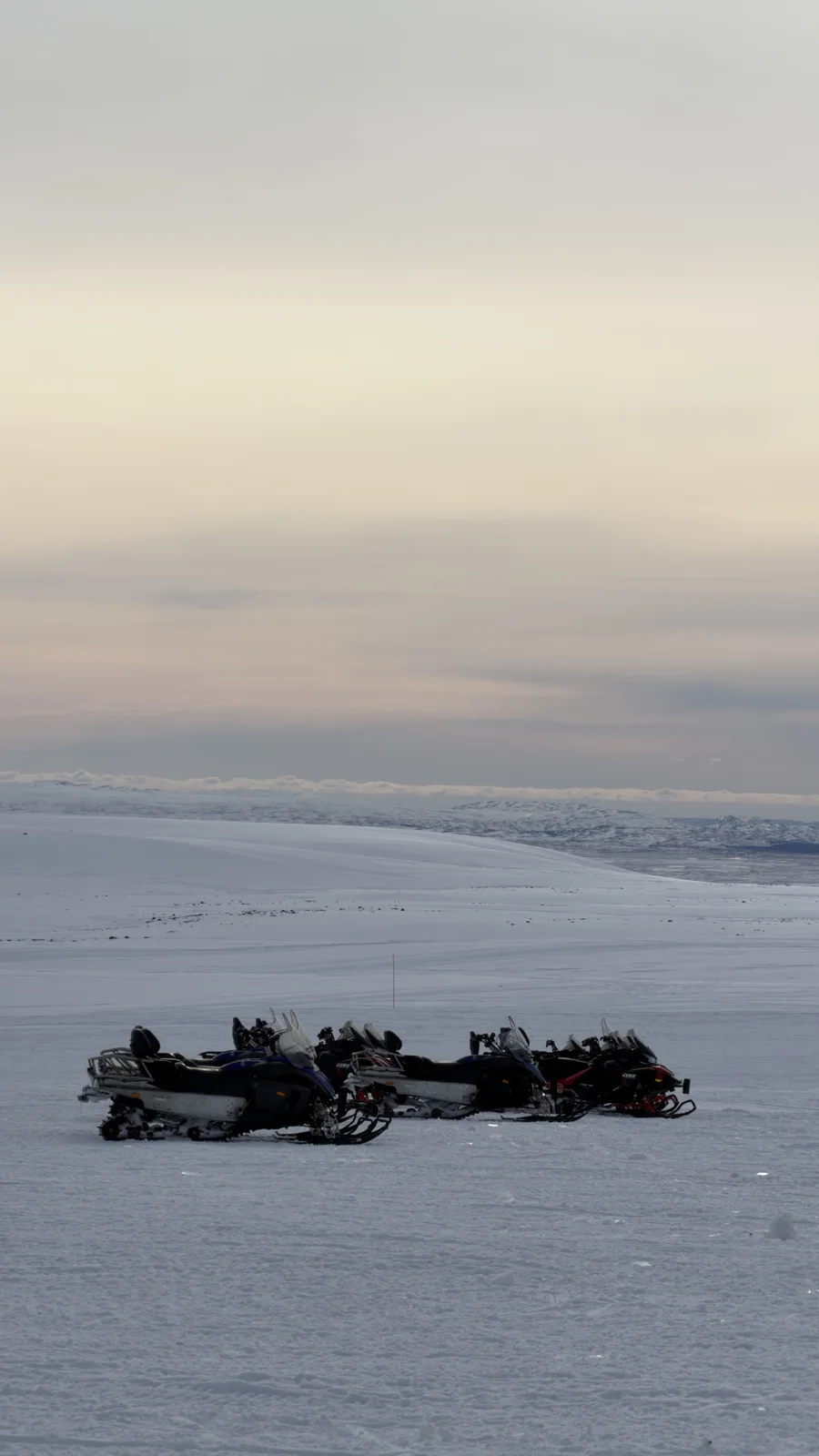 Glacier Snowmobiling — A distant line of snowmobiles on Langjökull beneath a pale sky