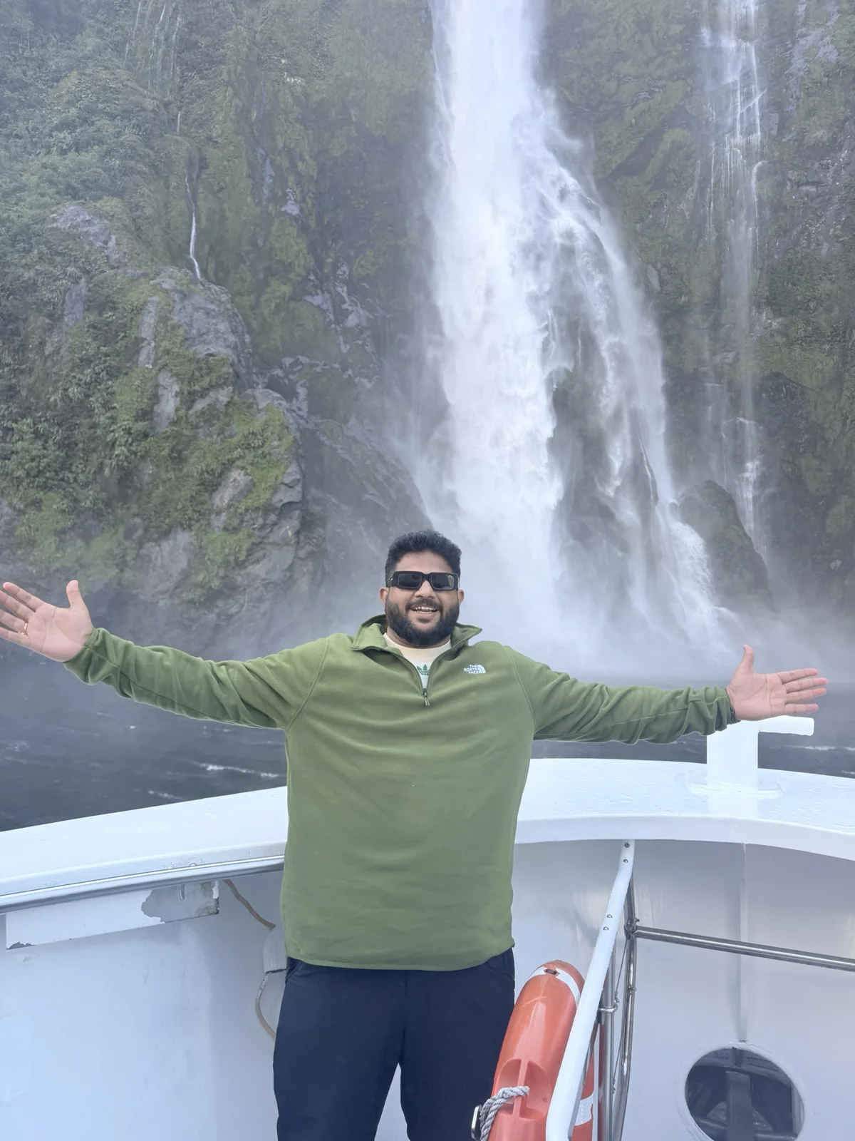 Milford Sound Flight & Cruise — A traveller on the boat deck with a waterfall behind him