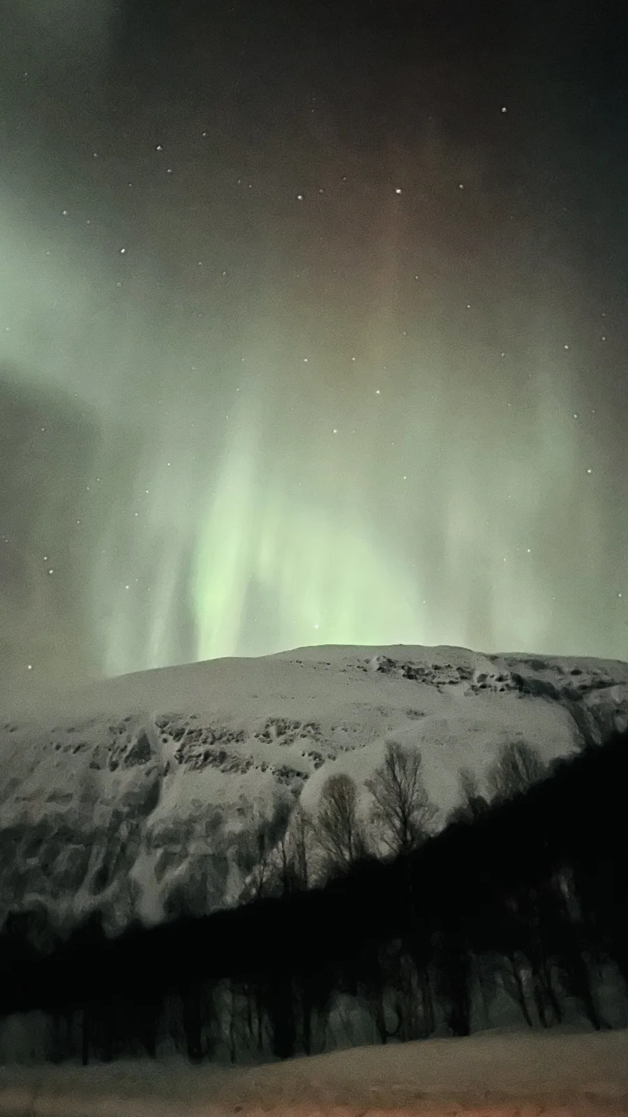 Northern Lights After Dark — Pale aurora curtains rising above a snowy mountain in the Tromsø region
