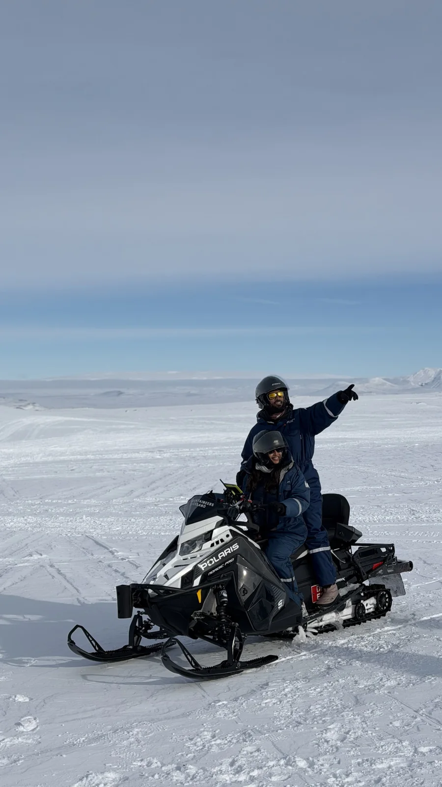 Glacier Snowmobiling — A traveller pointing across the glacier while seated on a snowmobile