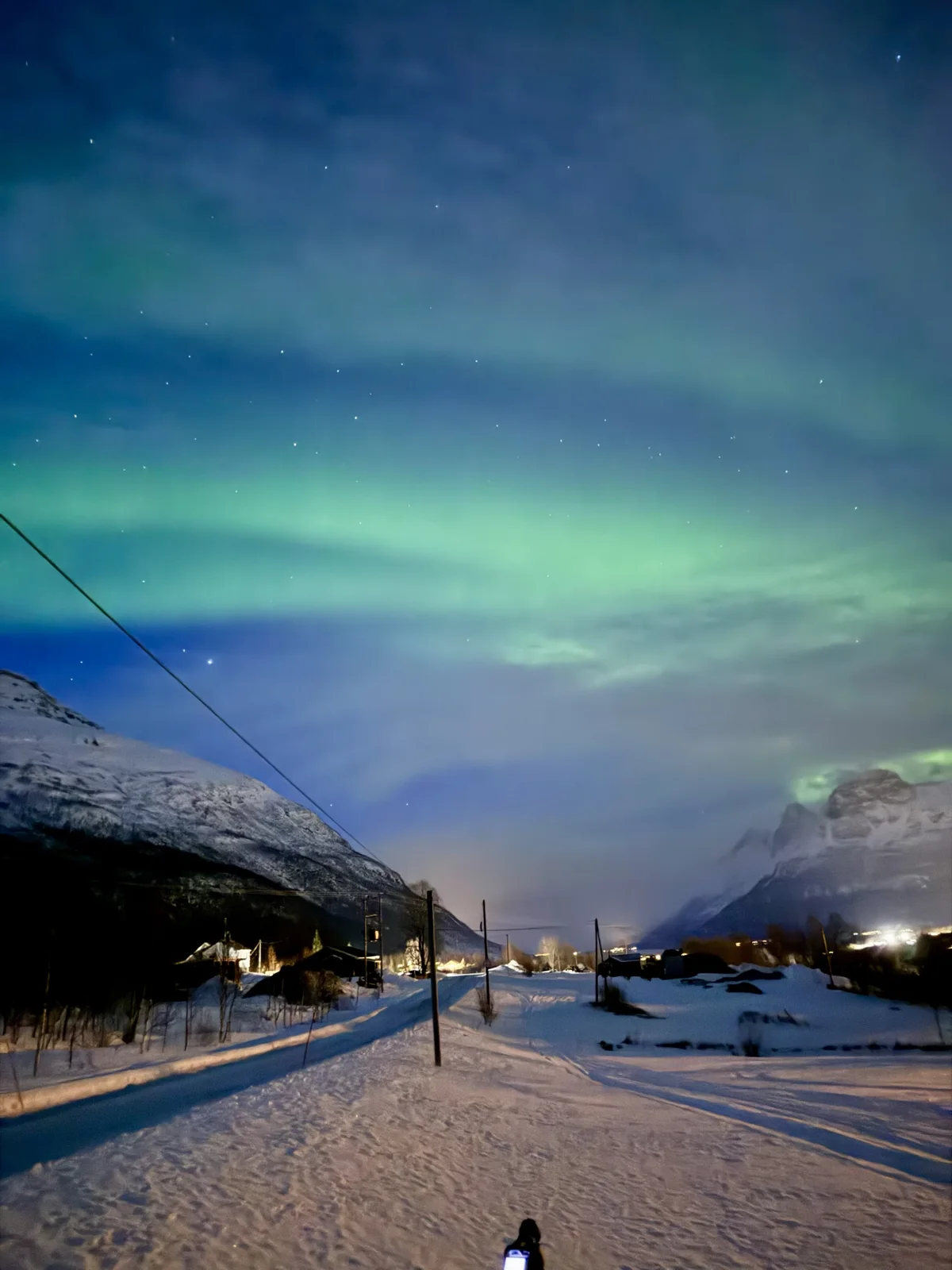 Northern Lights After Dark — Northern Lights above a snow-covered road and nearby hills