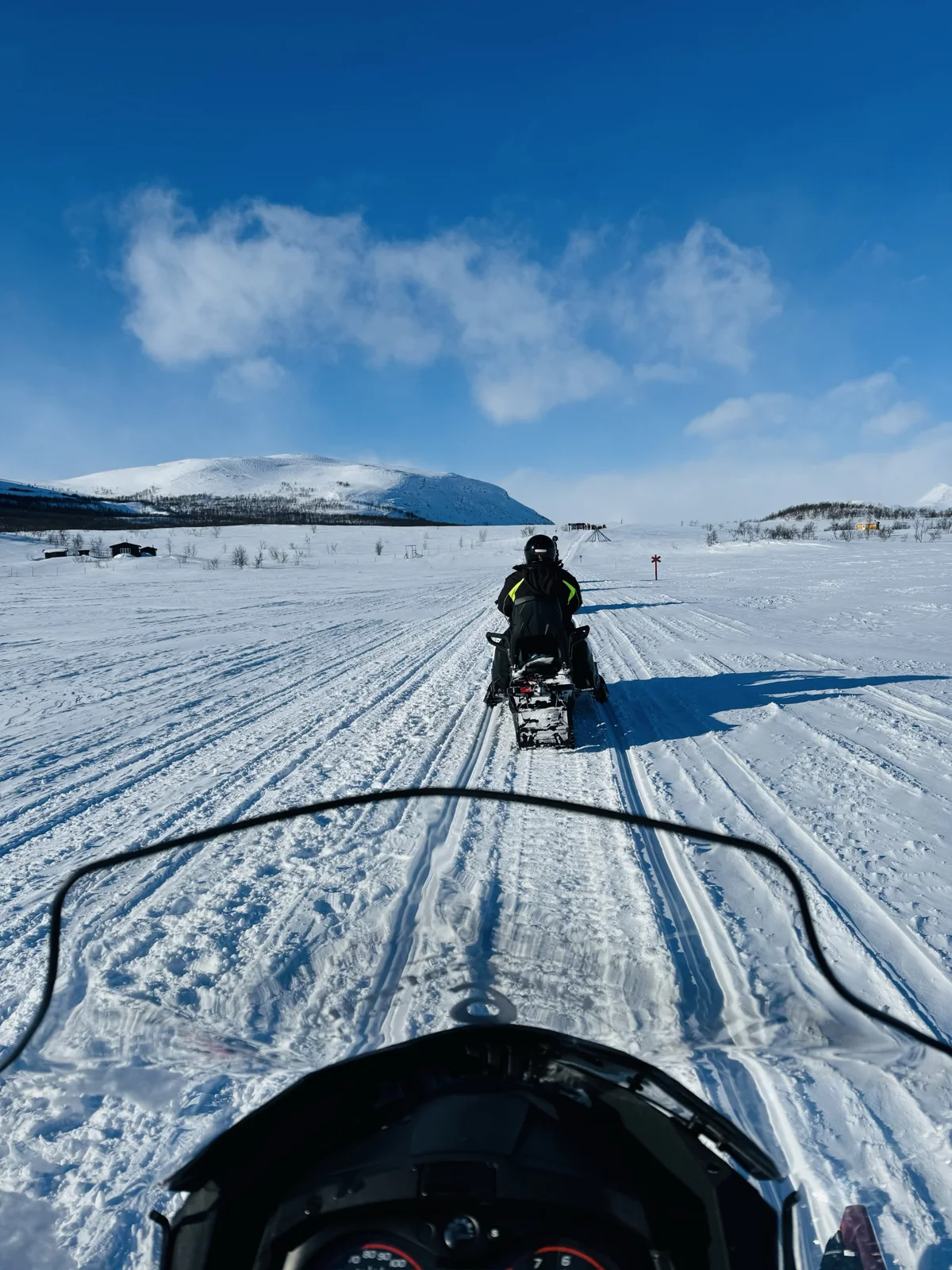 Snowmobile Safari — View over a snowmobile toward a rider ahead on a snowy trail